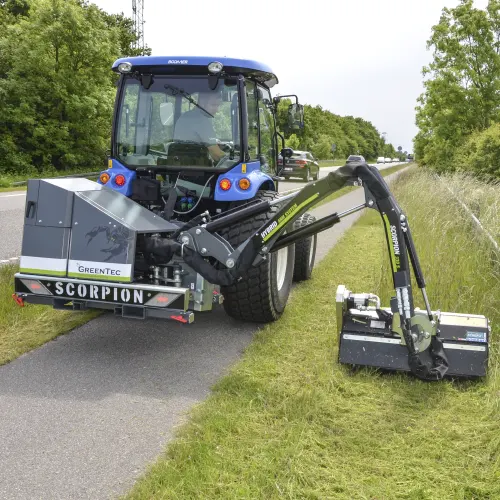 Compact tractor drives on bike path and mows grass in the side