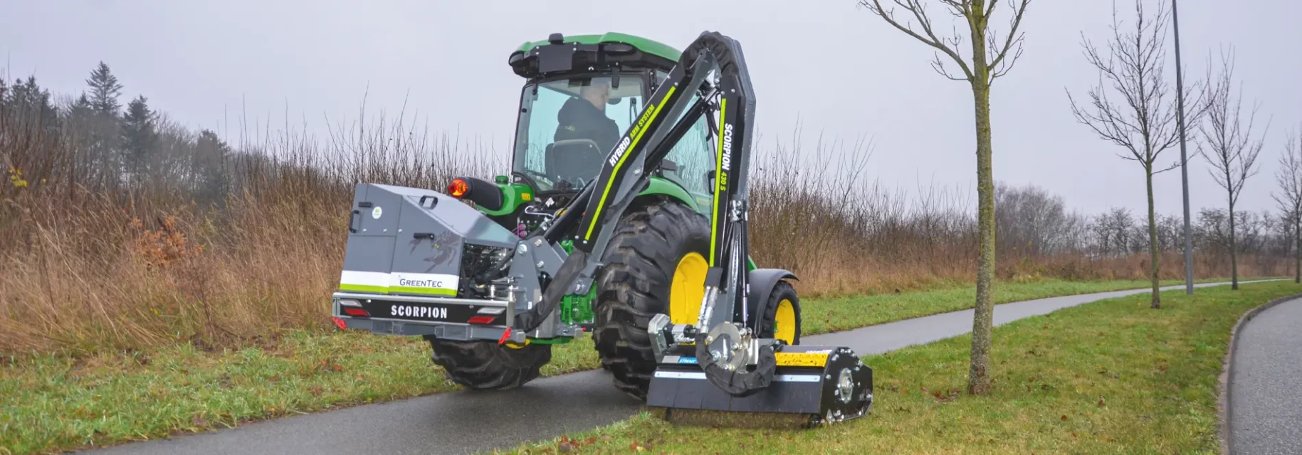 Small tractor with boom mower drives on bike path and mows grass in verges